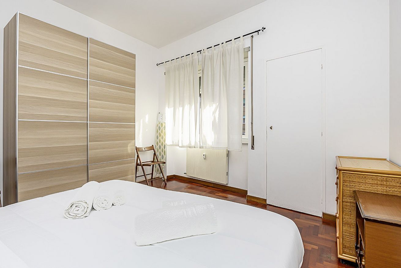 Une chambre à coucher comprenant un lit, une armoire, une chaise, une fenêtre avec des rideaux et un radiateur.