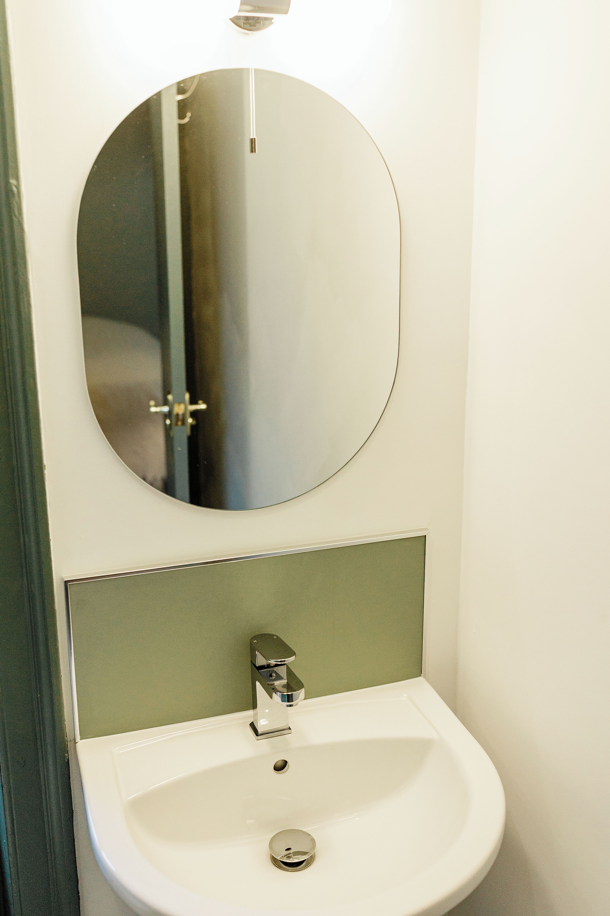 A bathroom with a round mirror above a white sink and a green wall.