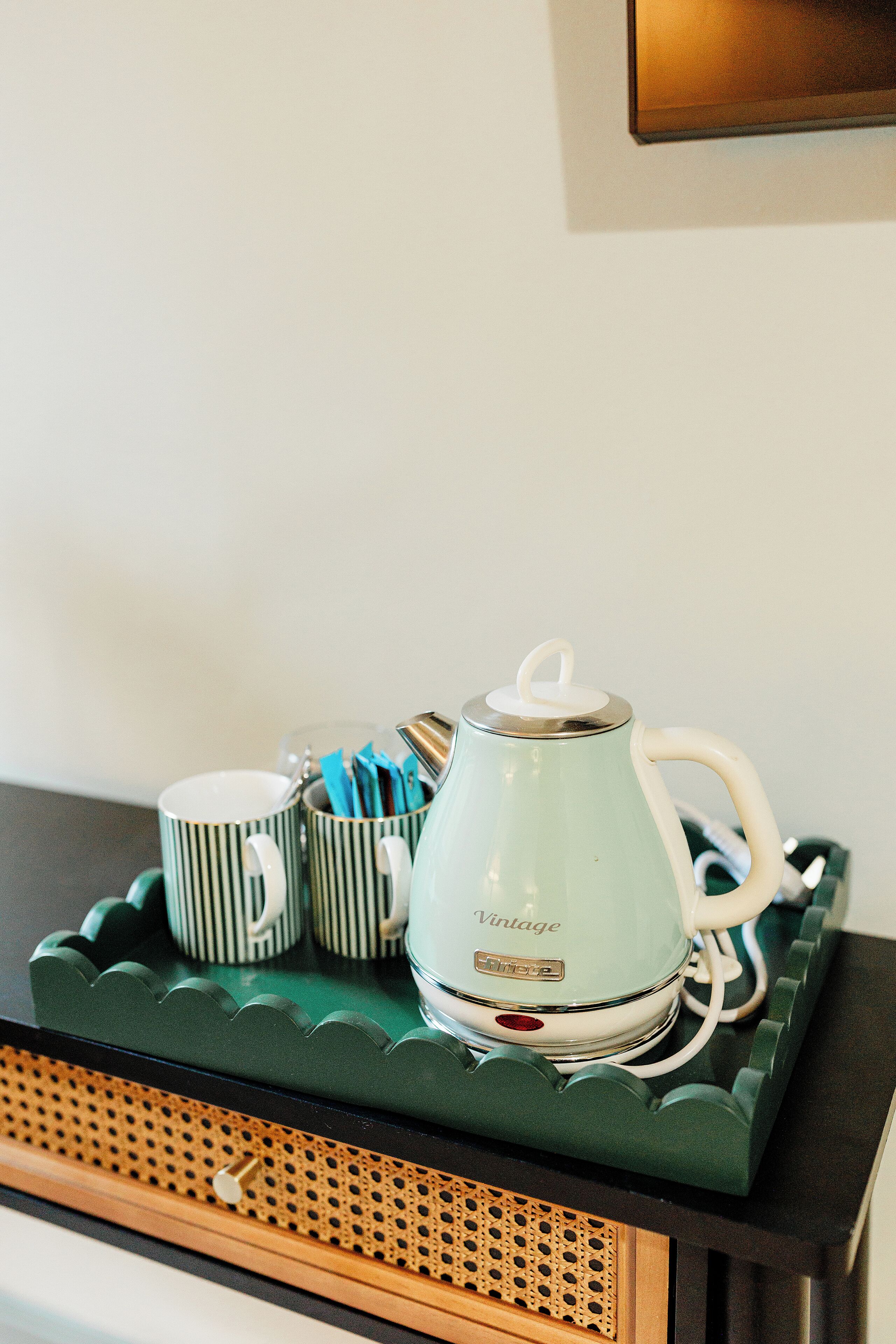 Una bandeja con un hervidor de estilo vintage, tazas a rayas y un reposa cucharas.