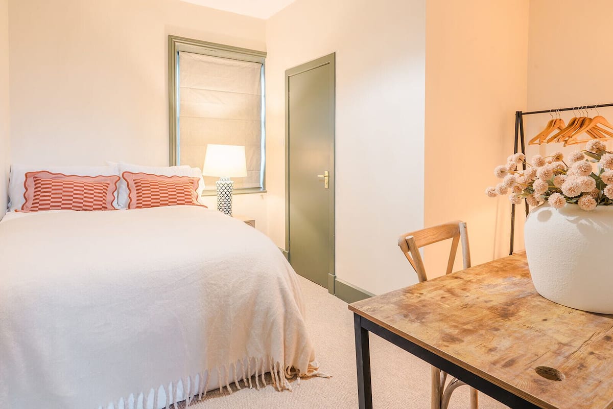 A hotel room with a bed, a table with a vase of flowers, a chair, a lamp, and a door.