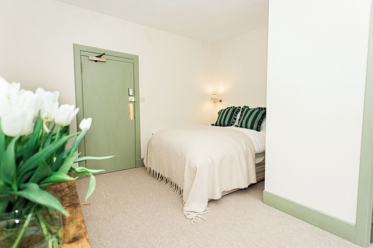 A bedroom with a bed, a green door, and a wall-mounted light fixture.