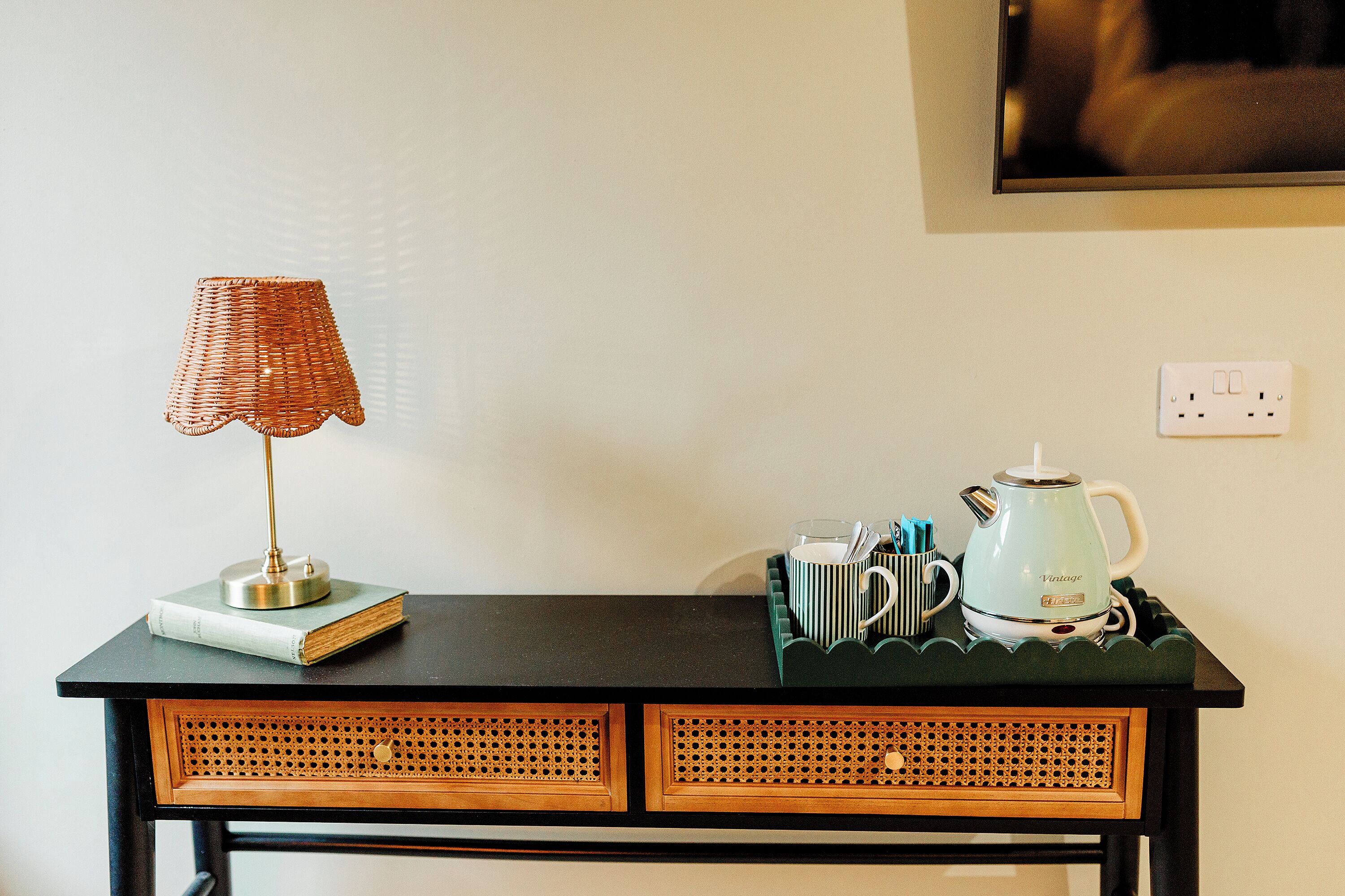 A desk with a lamp, a book, a mug, and a vintage-style kettle.