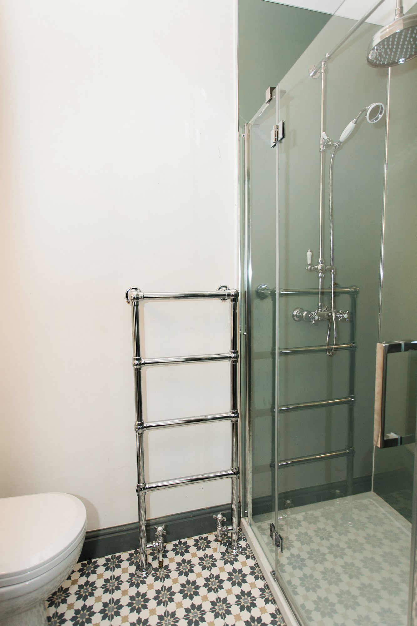 A bathroom with a glass shower enclosure, a chrome towel rack, and a toilet.