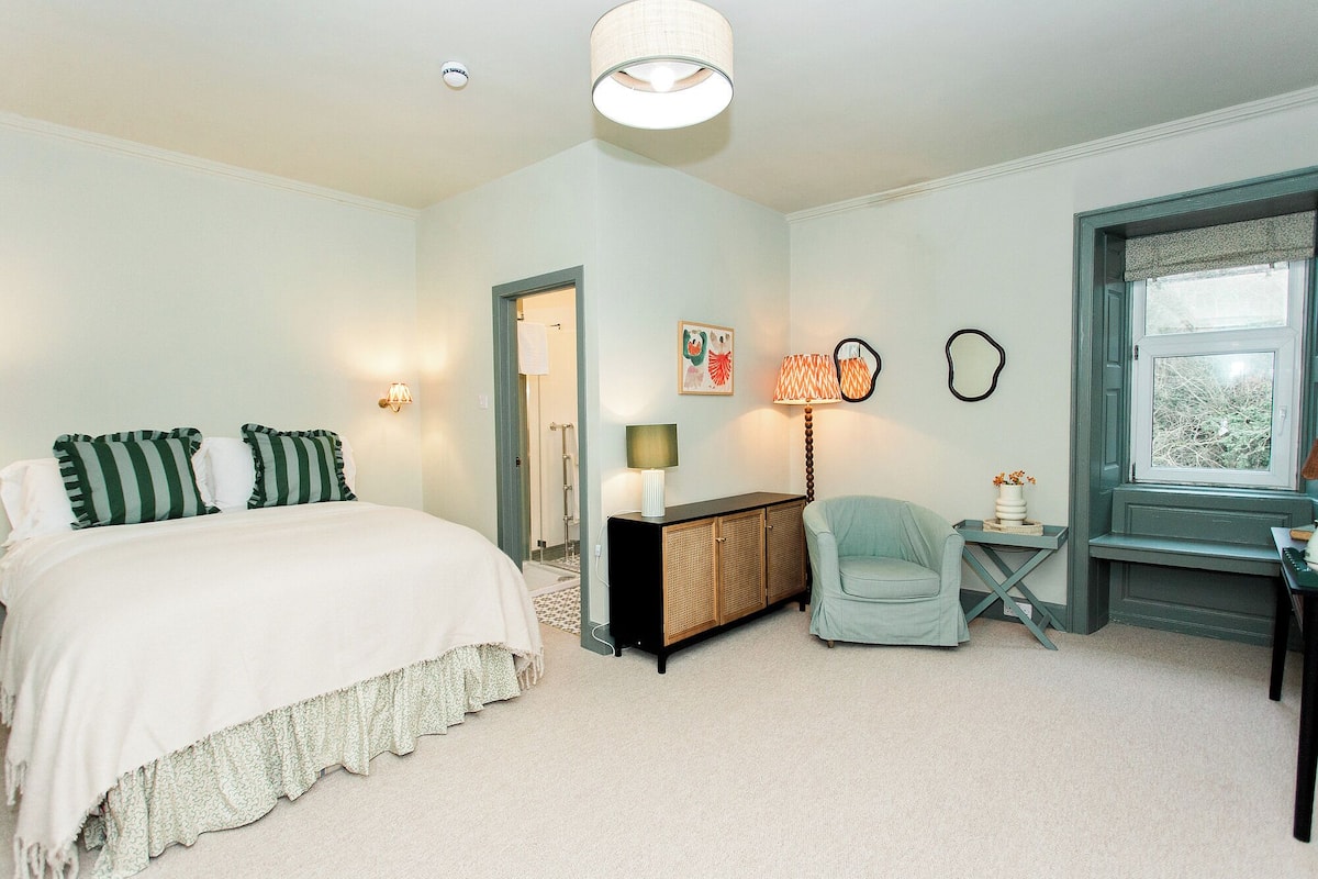 A bedroom with a bed, a desk, a chair, a lamp, and a window.