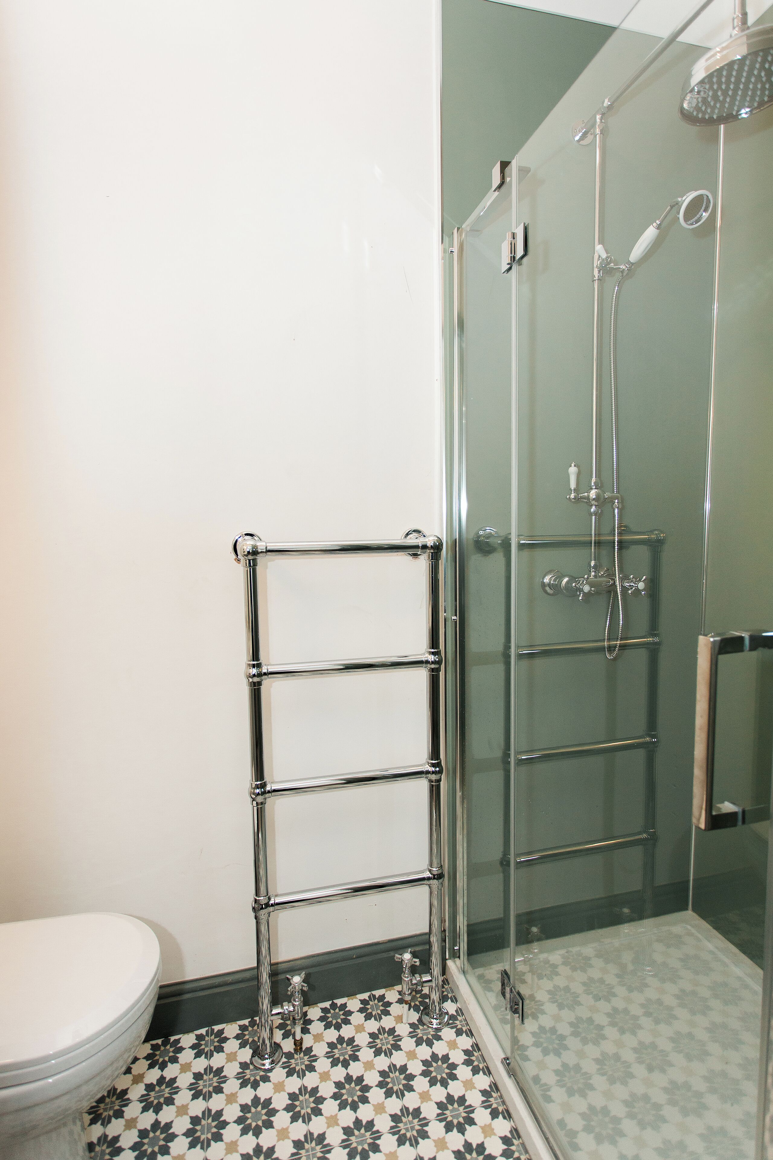 Un baño con ducha separada por mampara de cristal, un perchero de cromo y un inodoro.