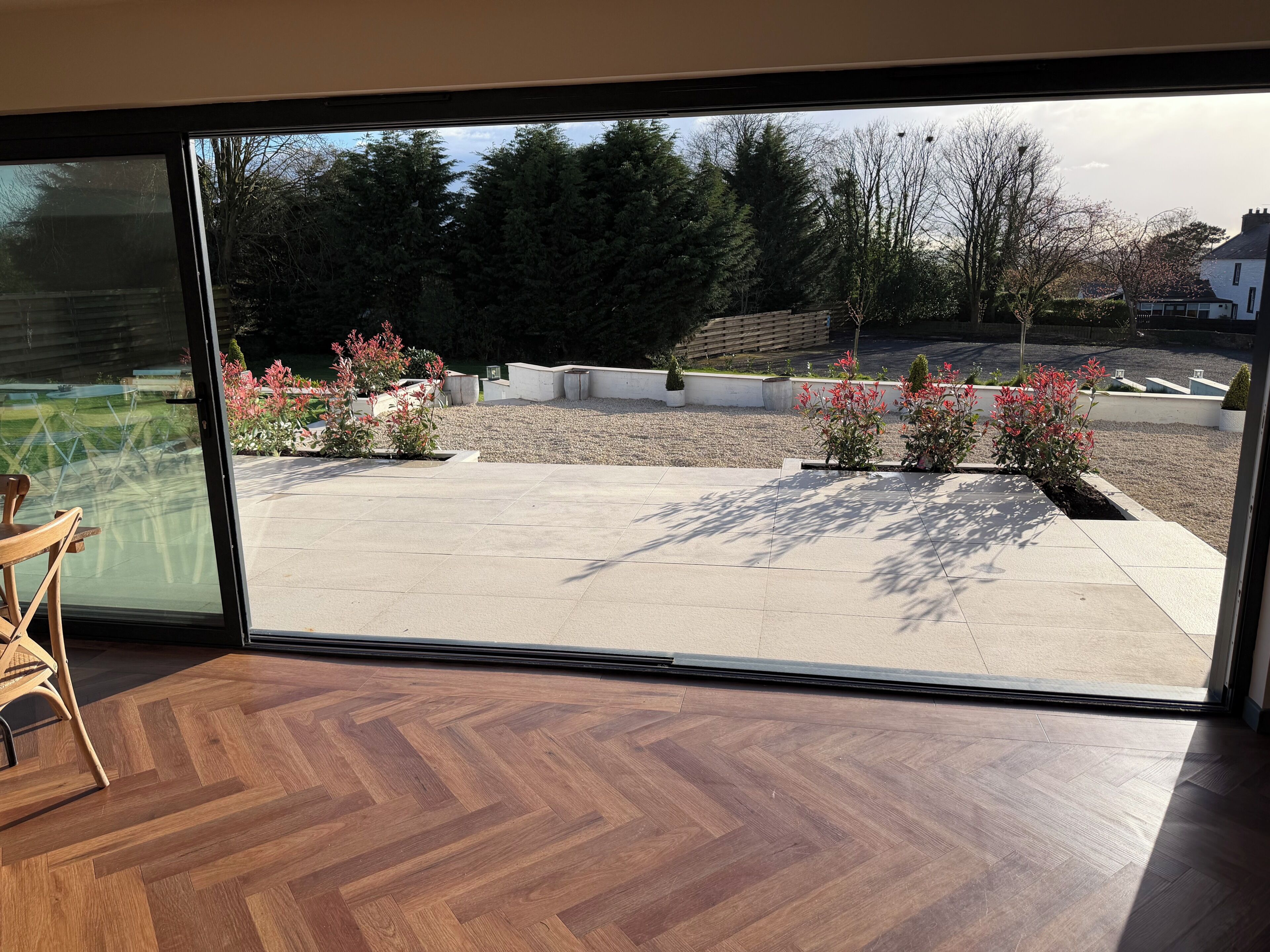 A room with a large sliding glass door leading to an outdoor patio with a herringbone floor and a view of a garden with shrubs and trees.