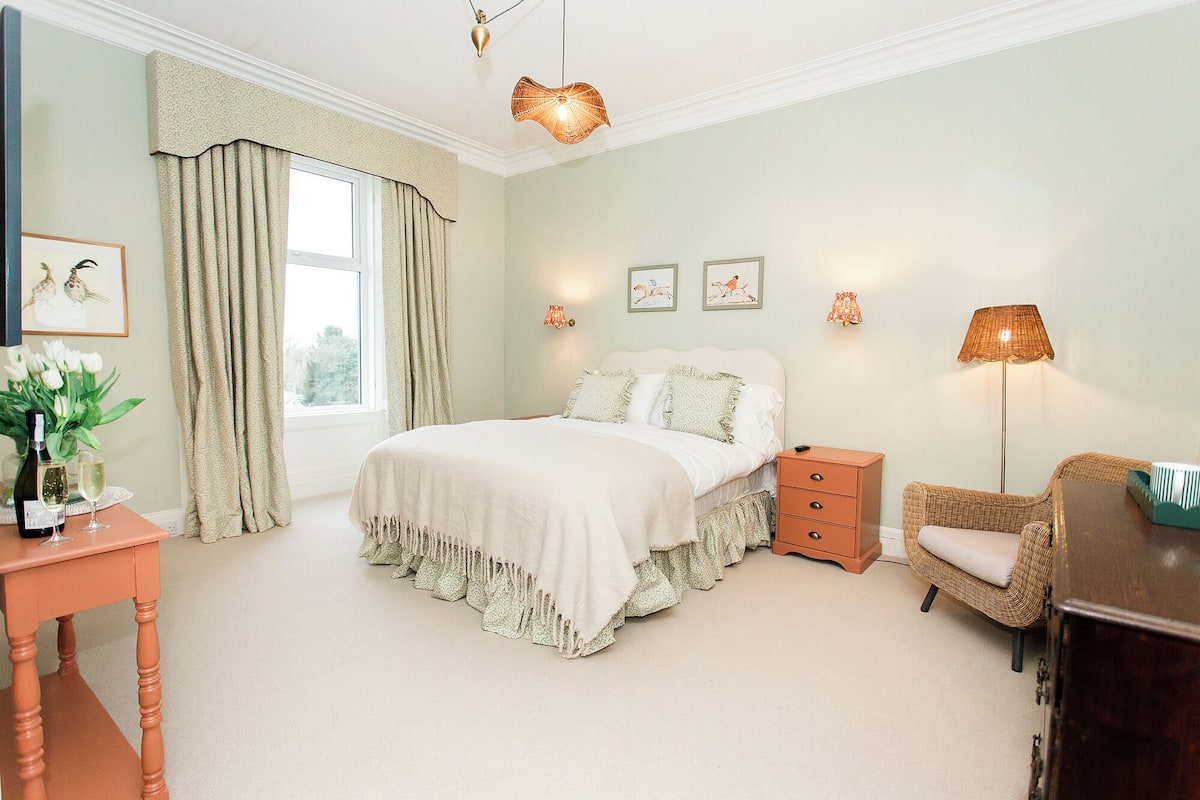 A bedroom with a bed, bedside table, chair, lamp, and artwork on the wall.