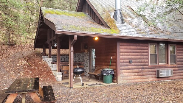 A rustic cabin with a stone fireplace, a covered porch, and a grill outside. - Adventurer's  Lodge, a charming 3-bedroom cabin with WiFi in quiet Lansing, WV. (Lansing)