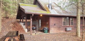 A rustic cabin with a stone fireplace, a covered porch, and a grill outside. - Adventurer's  Lodge, a charming 3-bedroom cabin with WiFi in quiet Lansing, WV. (Lansing)