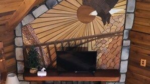 A stone fireplace with a TV above it, a red carpet, and a wooden ceiling. - Adventurer's  Lodge, a charming 3-bedroom cabin with WiFi in quiet Lansing, WV. (Lansing)