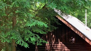 A rustic cabin with a stone foundation and a sloped roof, surrounded by dense green foliage. - Adventurer's  Lodge, a charming 3-bedroom cabin with WiFi in quiet Lansing, WV. (Lansing)