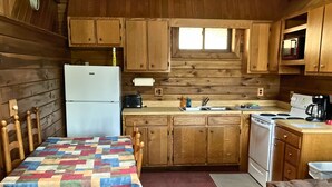 A cozy cabin-style kitchen with wooden cabinets, a refrigerator, a stove, and a dining table with chairs. - Adventurer's  Lodge, a charming 3-bedroom cabin with WiFi in quiet Lansing, WV. (Lansing)