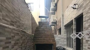 A narrow outdoor space with a brick wall, a small step leading to a door, and a metal rack on the right side. - MARESIAS BEACH - SP (Praia de Maresias São Sebastião)