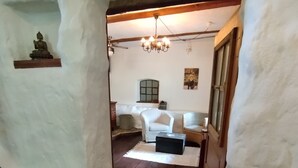 Un interno rustico con una scala in legno, una parete bianca con il numero 1659, una poltrona bianca, un baule di legno e un lampadario.