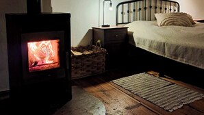 Un'accogliente stanza con un camino a legna, un letto con testiera, un comodino, uno specchio e una lampada.