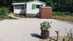 A small, single-story mobile home with a gravel driveway and a wooden shed.