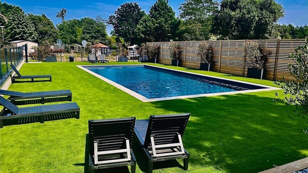 A rectangular swimming pool with a surrounding grassy area and two lounge chairs.