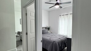 Une chambre à coucher avec un lit, un ventilateur de plafond, une table de chevet et une fenêtre avec des rideaux.