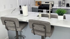 Une cuisine moderne avec des meubles gris, un four à micro-ondes en acier inoxydable, une cuisinière à gaz et deux tabourets de bar.