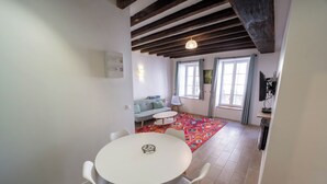 Ein Essbereich mit einem runden Tisch, vier Stühlen, einer Couch, einem gemusterten Teppich und einem Fenster mit Vorhängen.