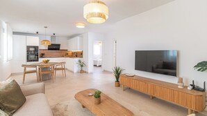A modern living room with a sofa, coffee table, TV, and a kitchen area in the background. - Villa Leyni Torrox by Ruralidays (Málaga)