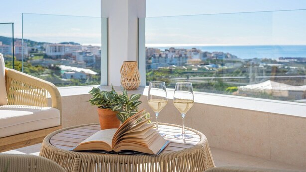 A balcony with a wicker chair, a potted plant, an open book, and two glasses of white wine. - Villa Leyni Torrox by Ruralidays (Málaga)
