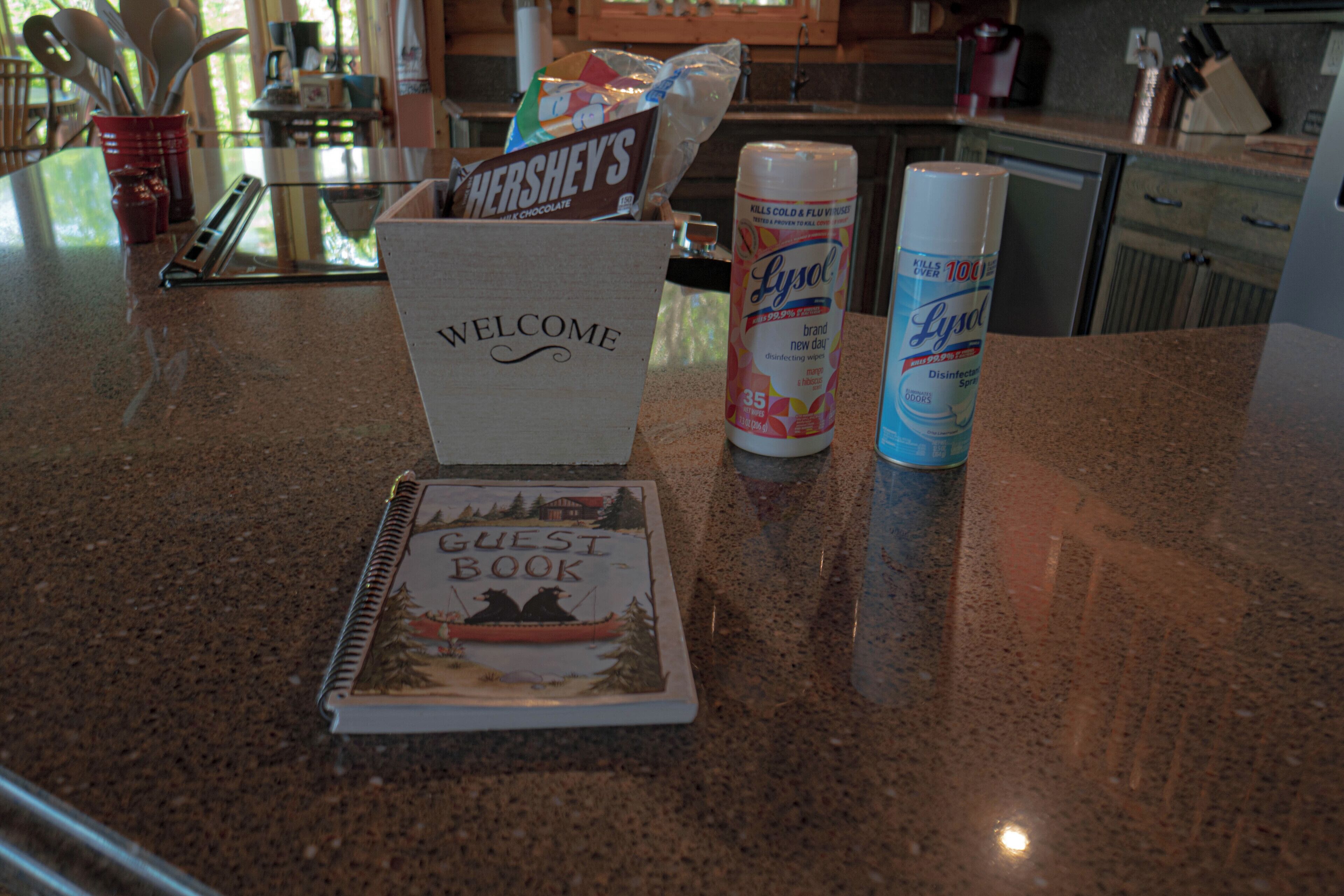 A kitchen counter with a welcome sign, a guest book, a can of Lysol disinfectant spray, and a bag of Hershey's chocolate.