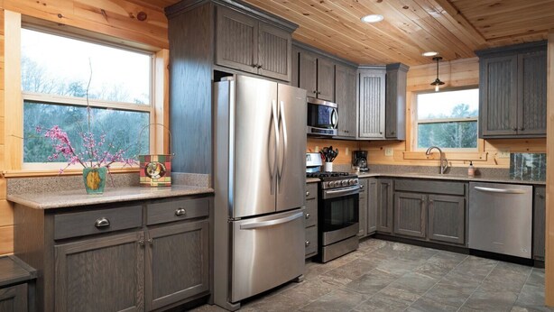 A modern kitchen with grey cabinets, stainless steel appliances, and a window with a view of trees.