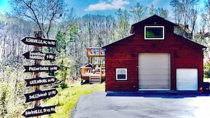 A rustic barn with a garage, surrounded by a wooded area. A directional signpost lists nearby towns and distances.