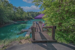 A wooden dock leading to a boat launch area with a covered seating area and a view of a river.