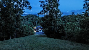 A rural house with a barn, surrounded by dense trees and a grassy field.