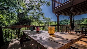 A wooden deck with a table and chairs, surrounded by a wooden railing, overlooking a forested area.