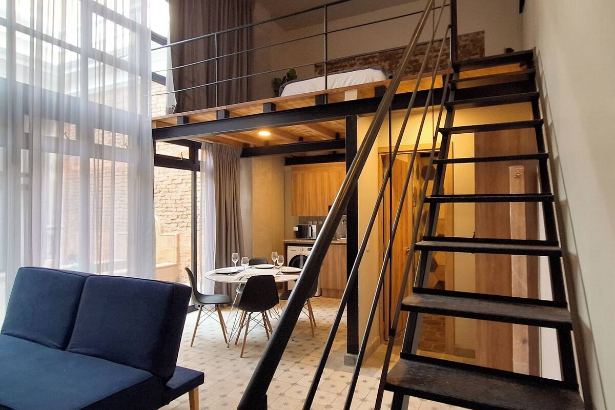 A modern room with a blue sofa, a dining area with a table and chairs, and a kitchen in the background.