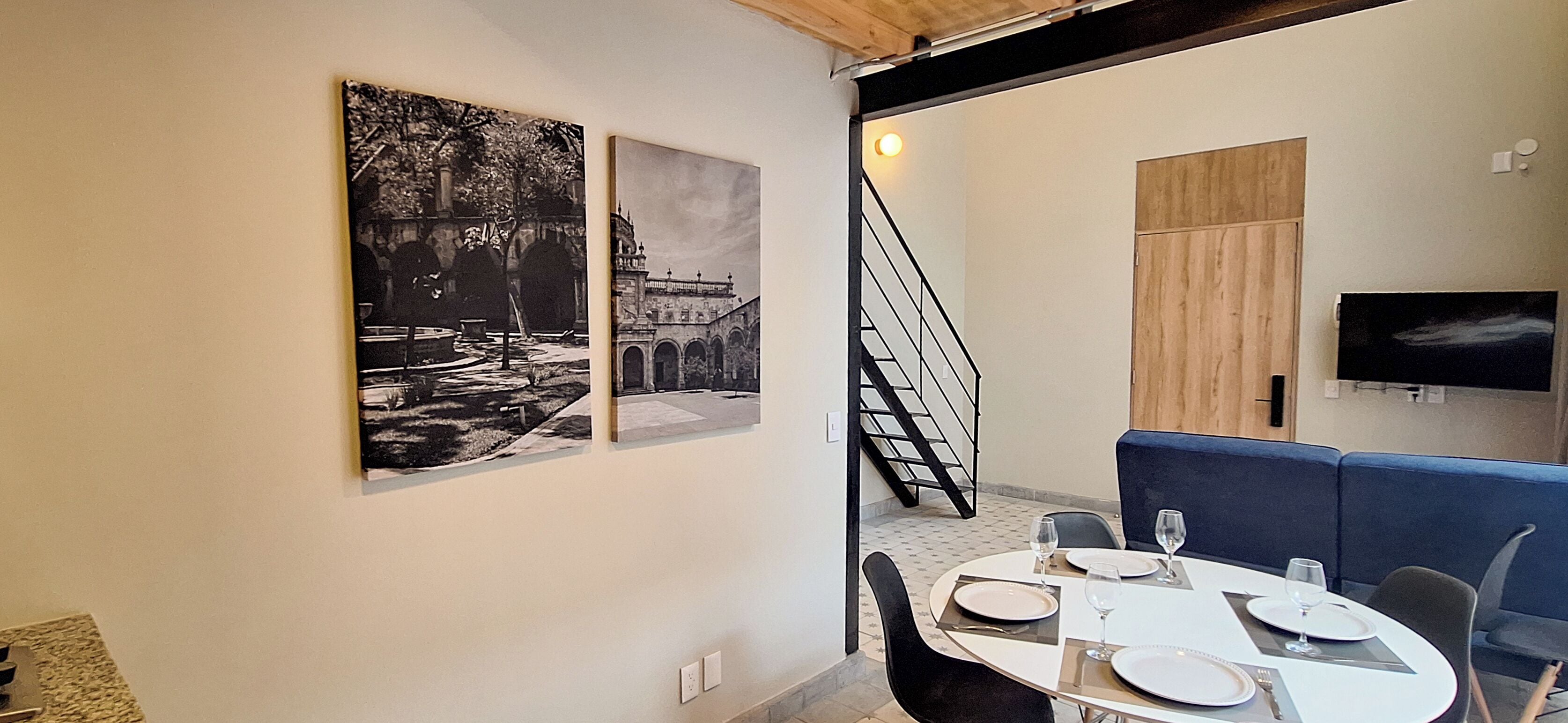 A dining area with a table set for four, a staircase, and two black-and-white photographs on the wall.