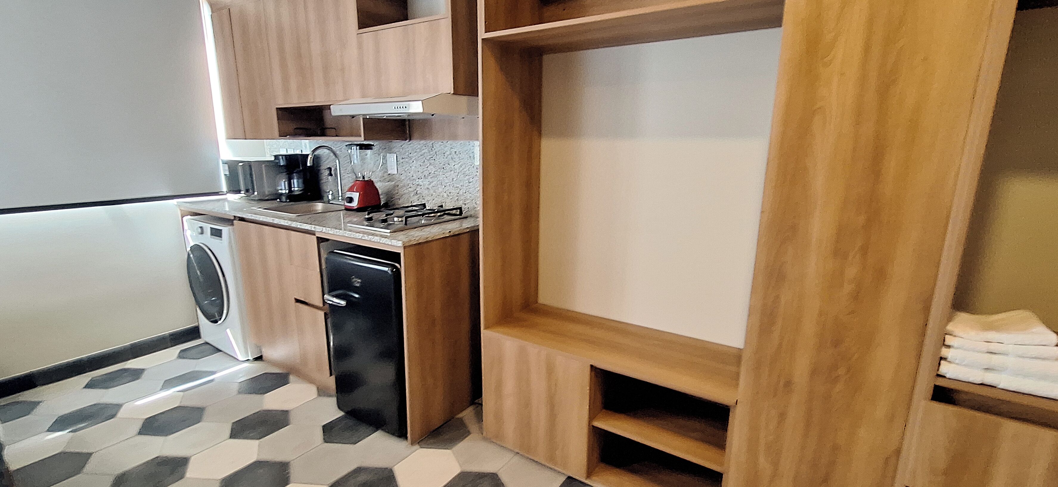 Cocina compacta con lavadora, cafetera y tetera roja.