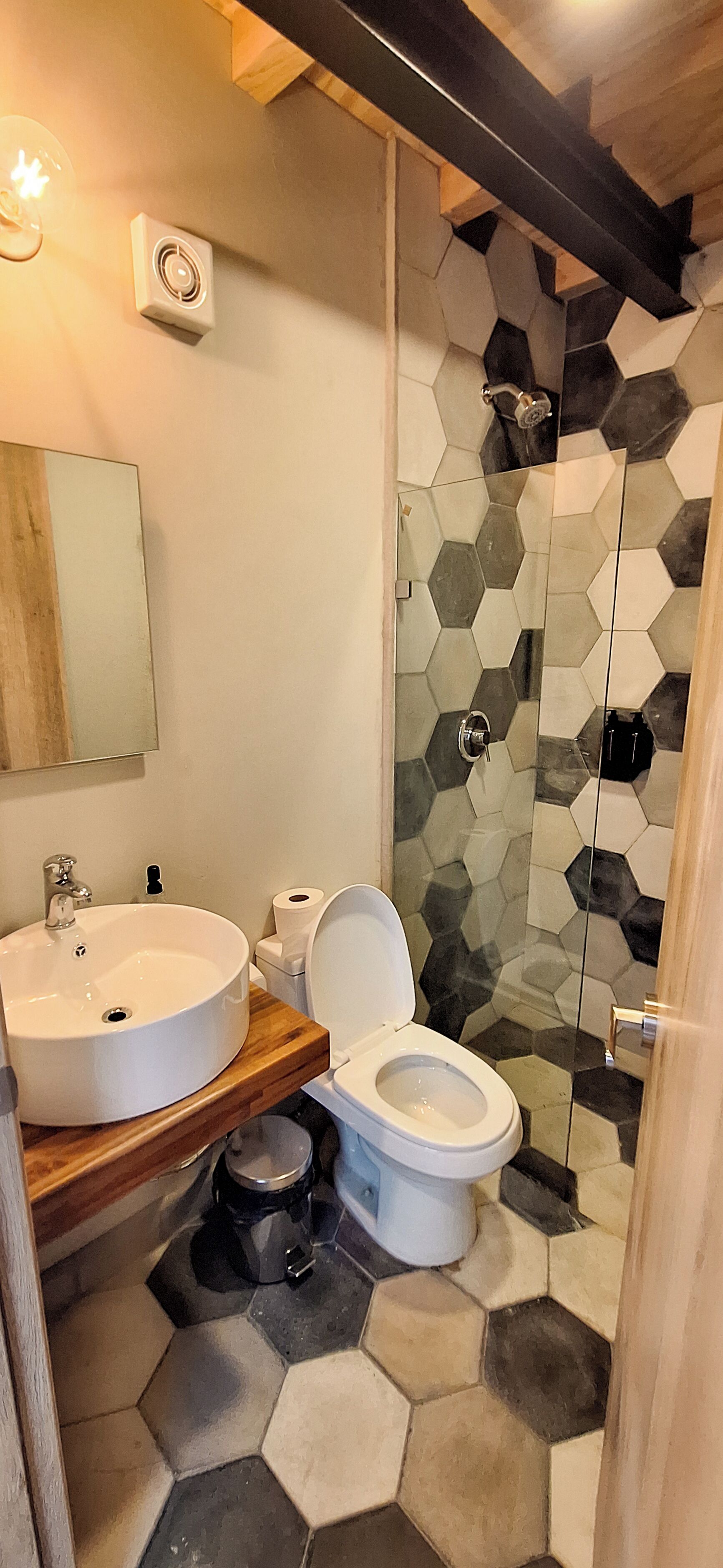 Un baño con un lavamanos redondo, inodoro y ducha. Las paredes tienen un patrón de baldosas hexagonales.