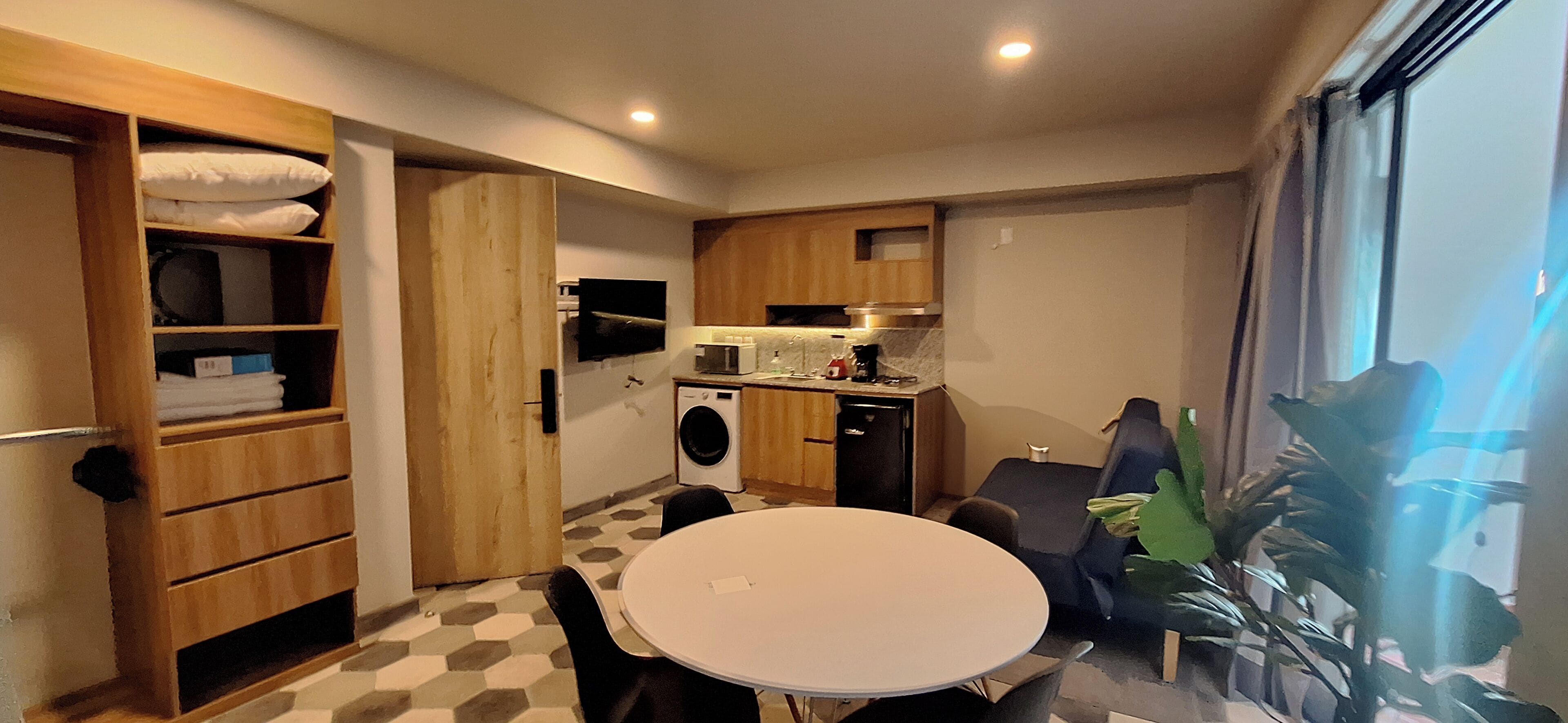 A compact kitchen with a dining area, a washing machine, and a TV.