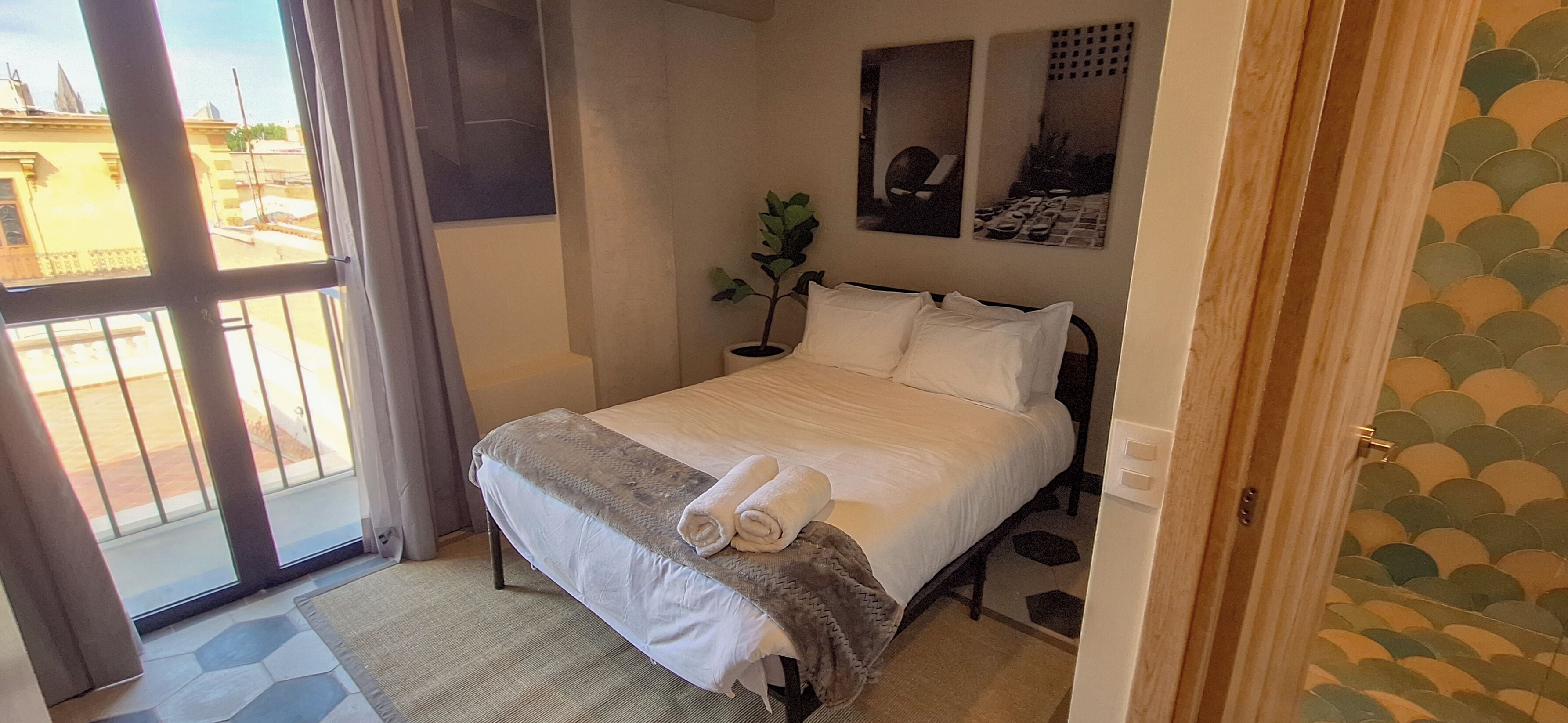 Ein Hotelzimmer mit einem Bett, einer Zimmerpflanze und Blick durch eine Glastür.