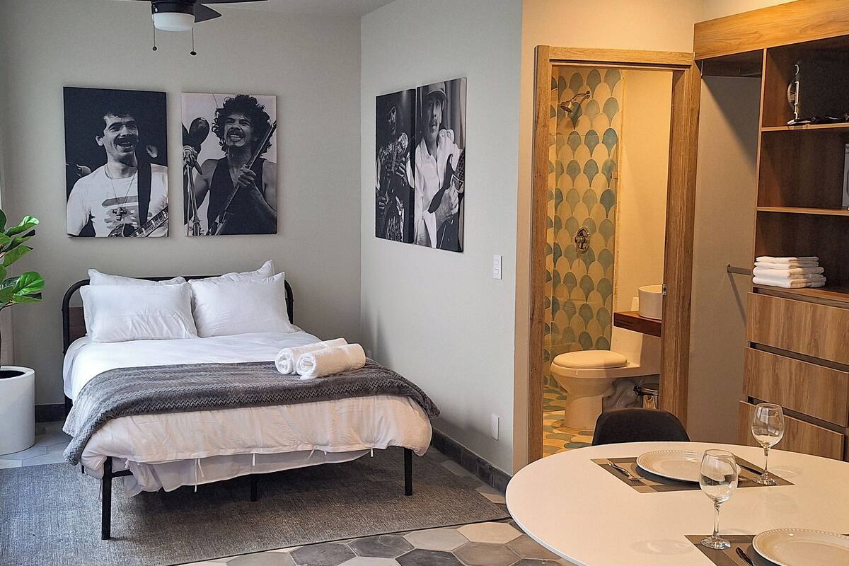 A hotel room with a bed, a small table with a wine glass, and a bathroom with a toilet and sink.