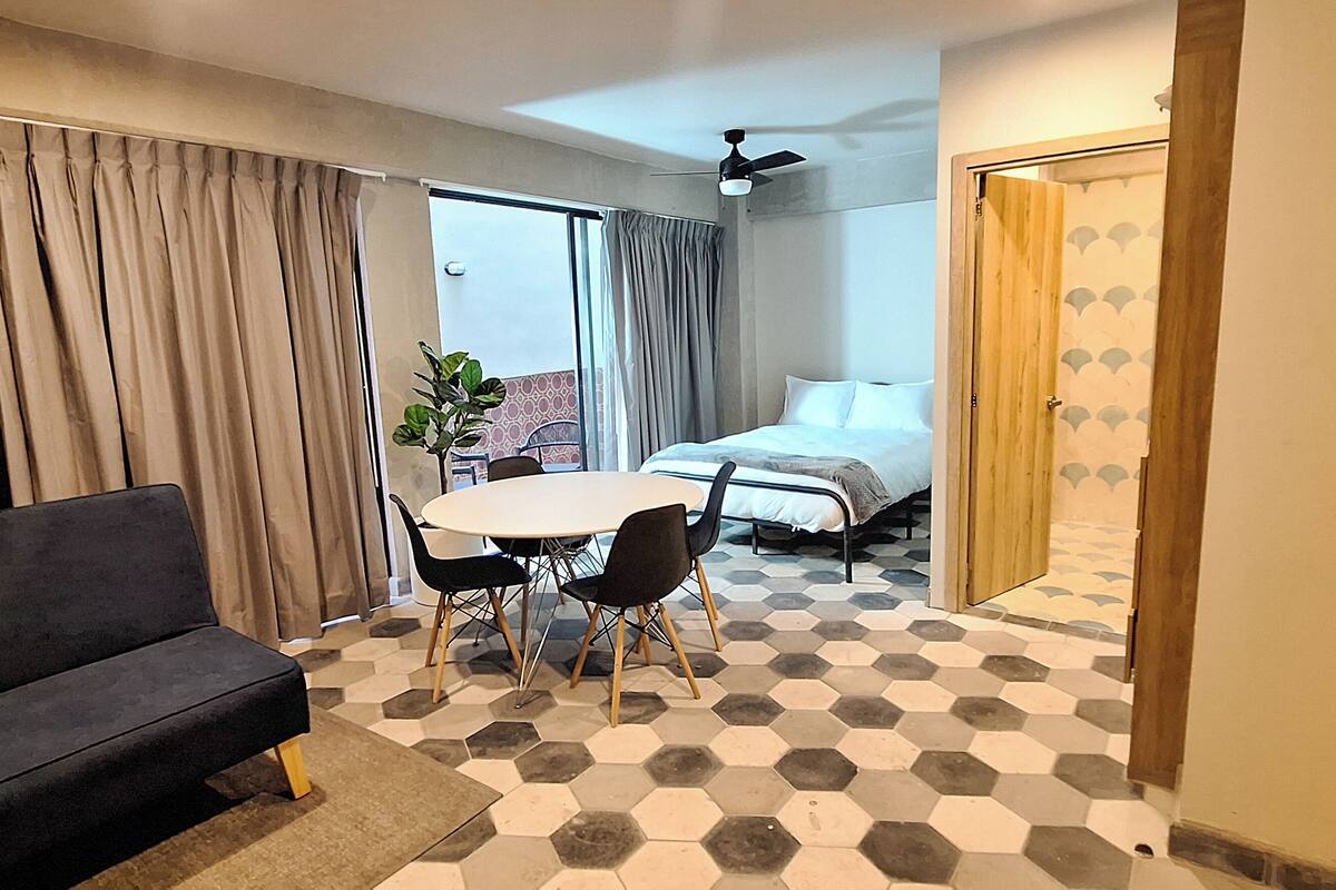 A hotel room with a sofa, a dining table with chairs, a bed, and a ceiling fan.