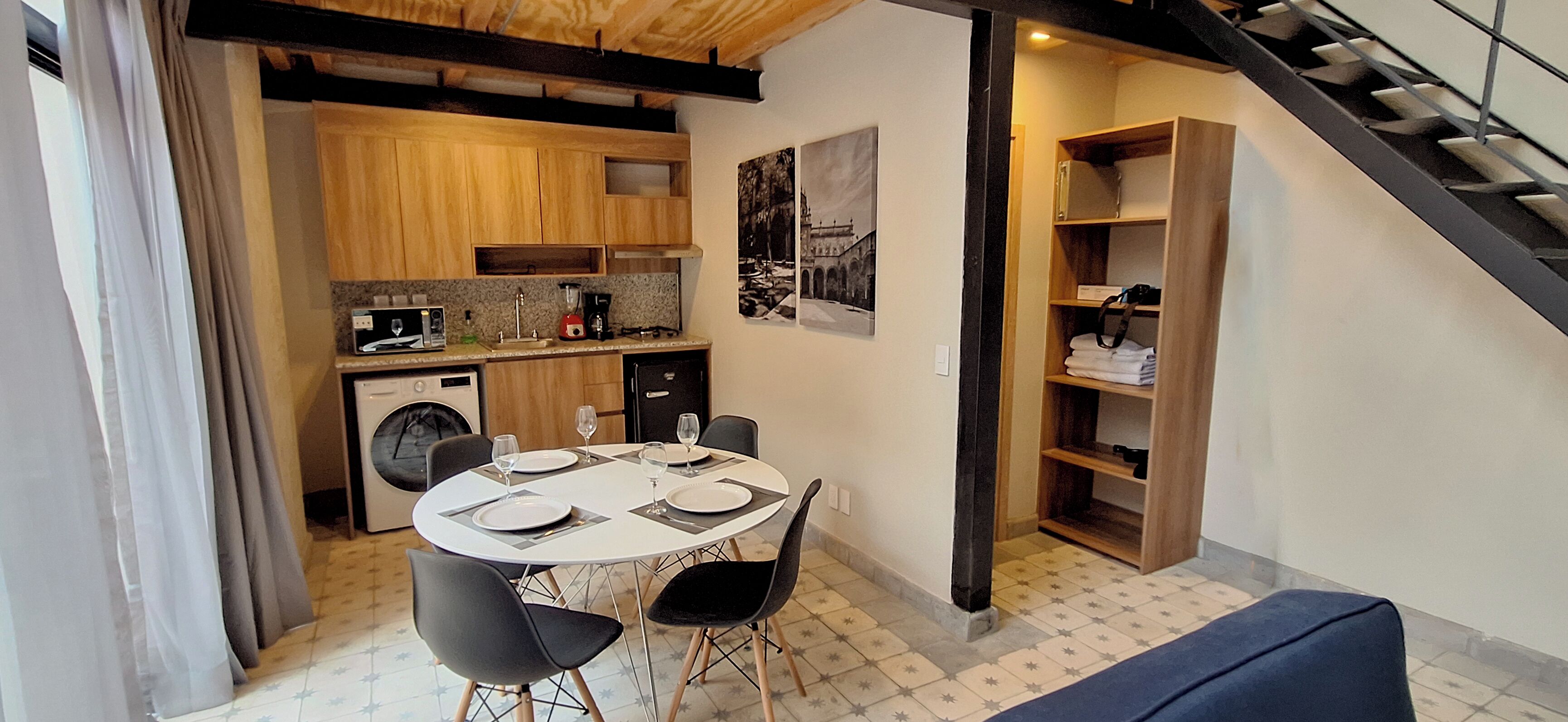 Une cuisine compacte avec des meubles en bois, une table à manger avec des chaises et un escalier menant à une mezzanine.
