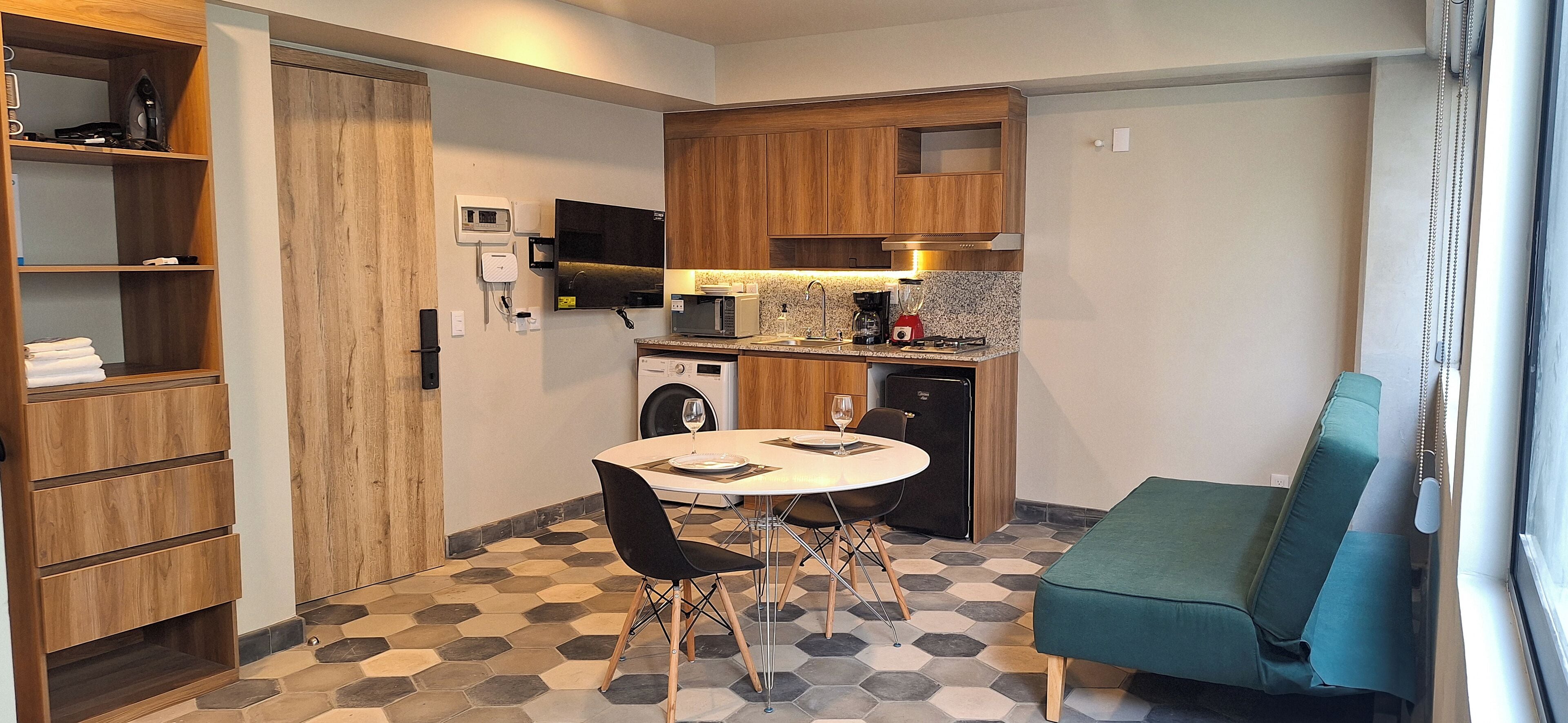 A compact kitchen with a microwave, toaster, and coffee maker, a washing machine, and a dining area with a table and chairs.