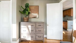 A room with a wooden floor, a grey dresser with drawers, a potted plant, and a framed picture on the wall.