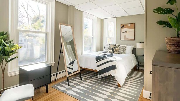 A modern bedroom with a bed, bedside tables, a mirror, and a large window.