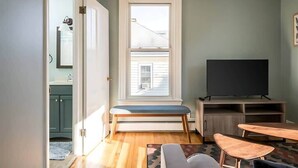A compact living space with a large window, a flat-screen TV, and a bench.