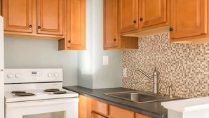 A kitchen with wooden cabinets, a white stove, a tiled backsplash, and a stainless steel sink.