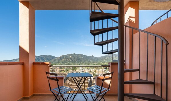 Un balcón con mesa y sillas, una escalera de caracol y vistas a montañas.