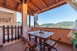 Een houten tafel met stoelen op een balkon, met uitzicht op bergen.