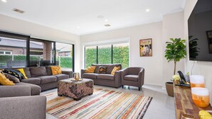A spacious living room with two sofas, a coffee table, and a large window offering a view of the outside. - Point Cook Serenity Stay (Point Cook)