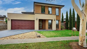 A modern two-story house with a red garage door, a well-maintained lawn, and a large tree in the foreground. - Point Cook Serenity Stay (Point Cook)